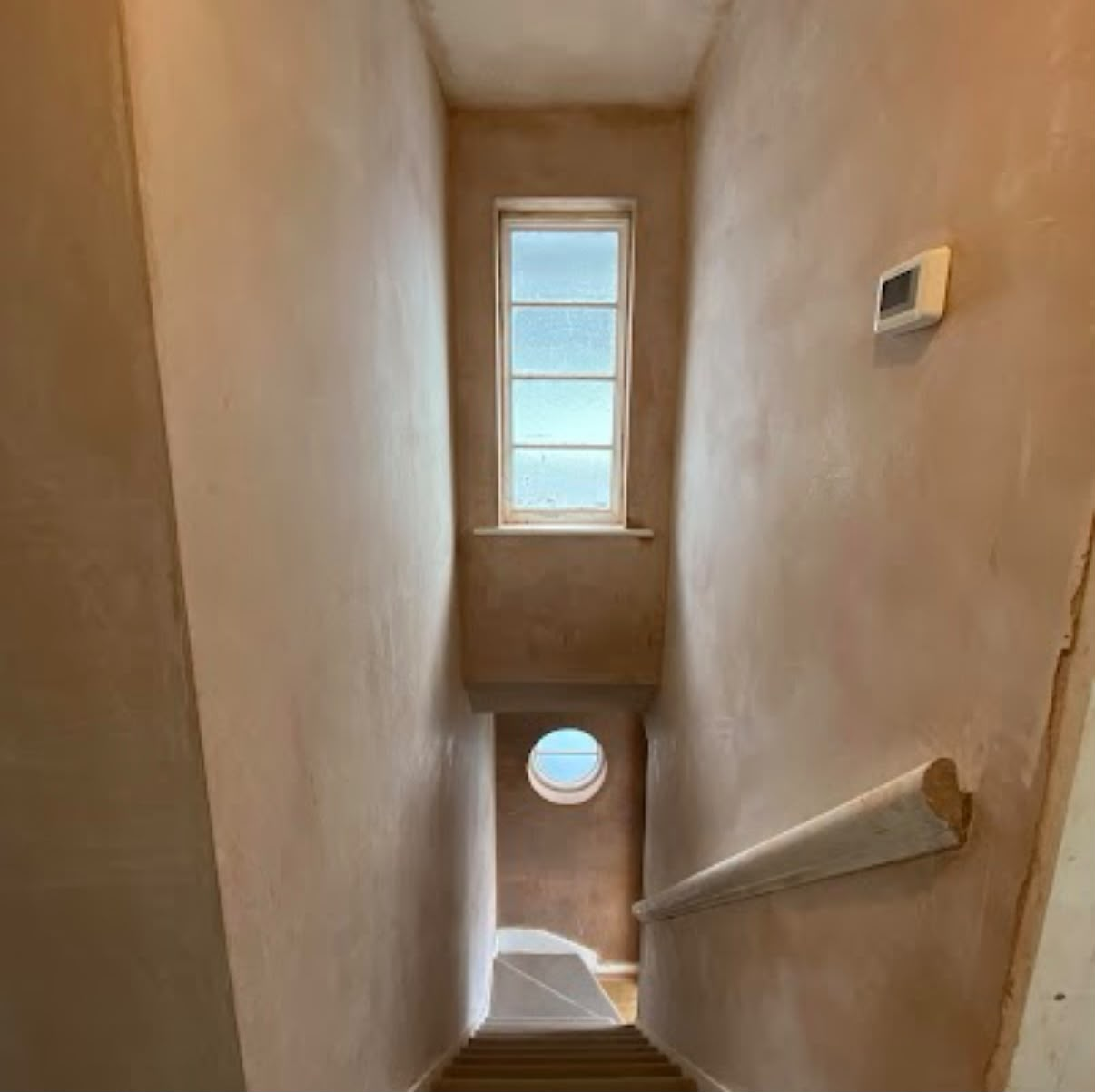 Narrow stairwell fully plastered with porthole window feature